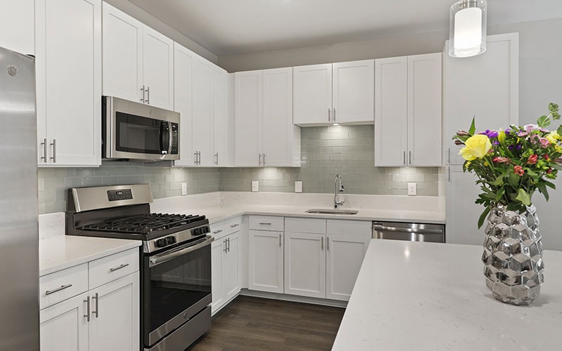 Spacious and well lit kitchen with wood floors and stainless steel appliances. 